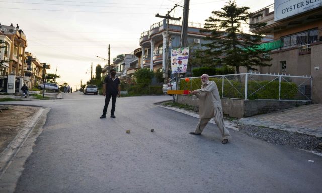 An elderly man plays cricket on a road in Islamabad