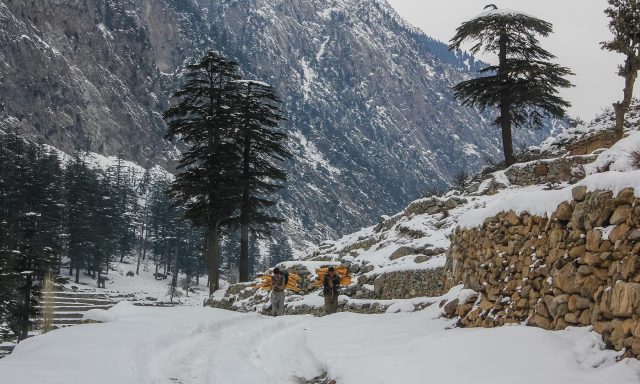 Two men carry firewood after heavy snowfall blankets Kalam valley