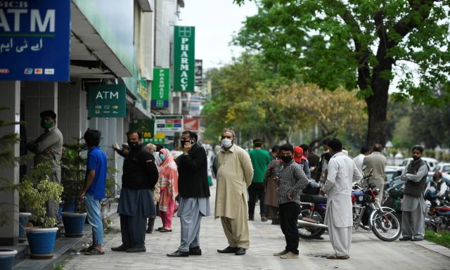 Residents wearing facemasks wait for their turn to withdraw money outside a bank in Islamabad